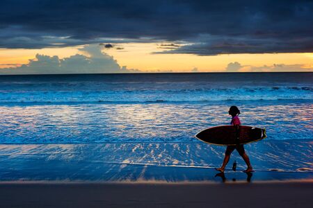 Surfgirl walking on the beach with surfboard at sunset. Bali islandの写真素材
