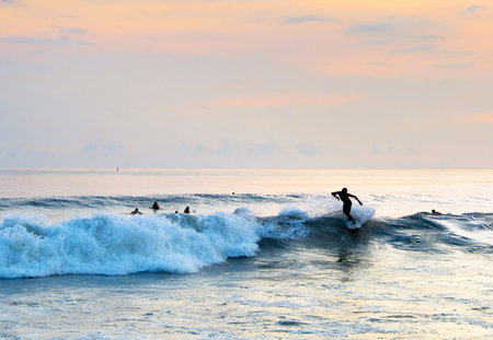 Surfer riding a wave in the ocean at sunset. Bali island
