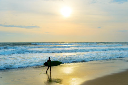 Silhouette of a local boy surfer walking on the beach. Bali island, Indonesia