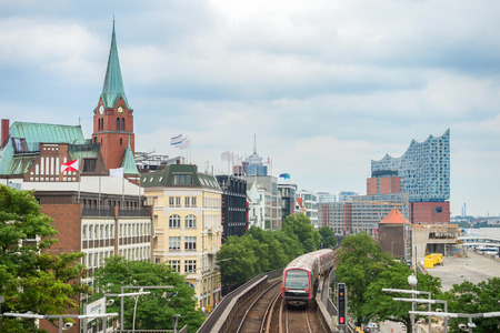 Metro train passing by Hamburg embankment with clock tower and Elbphilharmonie building at background, Germanyの写真素材