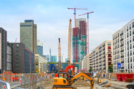 Excavator, cranes and construction equipment at construction site in downtown at street with buildings and skyscaraprers of modern architecture, Frankfurt am Main, Germanyの写真素材