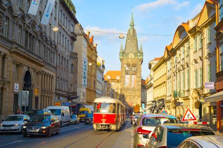 PRAGUE, CZECH REPUBLIC - NOVEMBER 14, 2018: Sunshine in Prague old town street, red tram and car traffic, Henri Bell tower in backgroundのeditorial素材