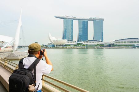 SINGAPORE - JANUARY 14, 2017: Rear view of tourist with backpack taking picture of Marina Bay Sands Resort and Artscience museum - famous landmarks of Singaporeのeditorial素材