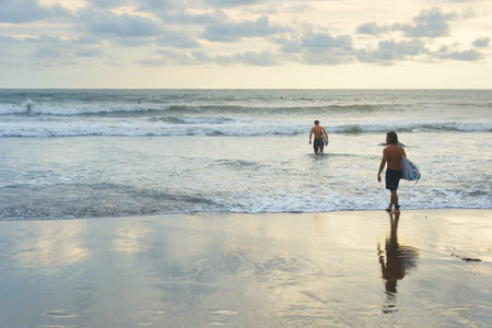 BALI ISLAND, INDONESIA - FEBRUARY 12, 2017: Men with surfboards at sunset ocean beach going for surf...