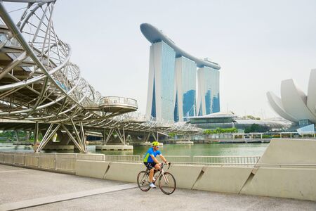 SINGAPORE - JANUARY 14, 2017: Cyclist riding bicycle, Singapore Marina Bay, ArtScience Museum and Helix bridge in backgroundのeditorial素材