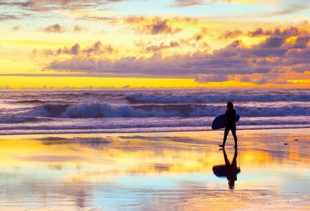 Surfer walking by the beach with surfboard at sunset. Bali, Indonesiaの写真素材