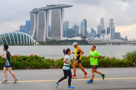 SINGAPORE - FEBRUARY 16, 2017: People running by the embankment of Singapore river in front of Singapore Donwtownのeditorial素材