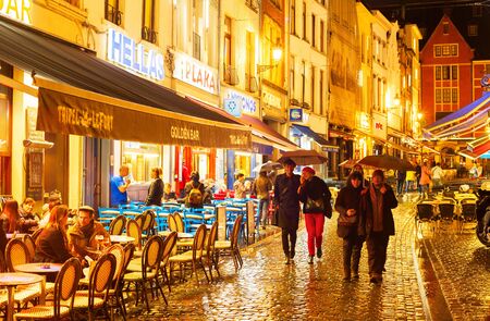 BRUSSELS, BELGIUM - OCTOBER 07, 2019: People walking and sitting at a restaurant on Old Town shopping street of Brussels in the rain at twilightのeditorial素材