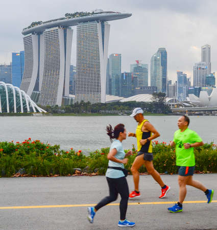 SINGAPORE - FEBRUARY 16, 2017: People running by the embankment of Singapore river in front of Singapore Donwtownのeditorial素材