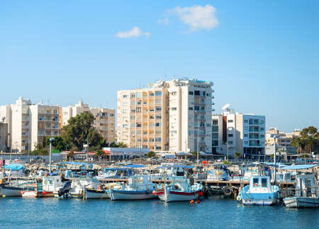 Larnaca marina with motor boats and yachts in bright sunlight, modern resort cityscape with apartments by the sea in background, Cyprusのeditorial素材