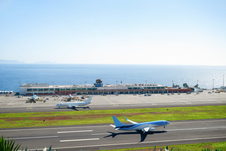 Aerial view of airplaine taking off runway at Madeira international airport, airplanes by terminal building and seascape in background, Portugalのeditorial素材