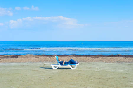 LARNACA, CYPRUS - FEB 18, 2019: Woman taking sunbathes on a deserted beach. Cyprus is a famous tourist destination.のeditorial素材