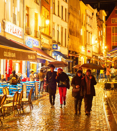 BRUSSELS, BELGIUM - OCTOBER 07, 2019: People walking and sitting at a restaurant on Old Town shopping street of Brussels in the rain at twilightのeditorial素材