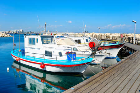 White motorboats reflecting in water, wooden pier, marina of Larnaca in bright sunshine day, Cyprusの写真素材