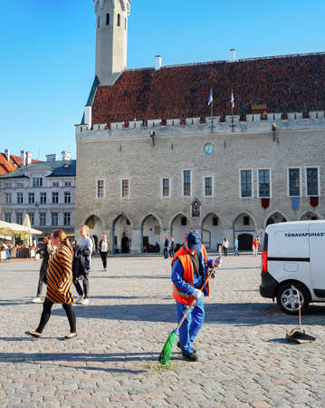 TALLINN, ESTONIA - JULY 14, 2019: Man sweeping central Town Hall Square, walking tourists, old town cityscape in bright sunlightのeditorial素材