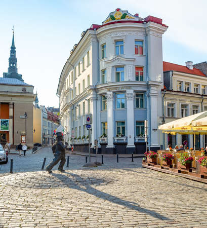 TALLINN, ESTONIA - JULY 14, 2019: Tourists sitting in street restaurant in old town of Tallinn, statue of walking man and cityscape in evening sunshineのeditorial素材