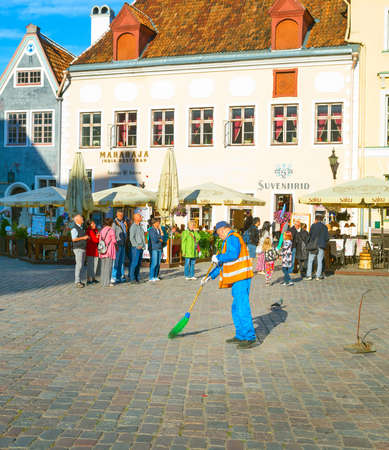 TALLINN, ESTONIA - JULY 14, 2019: Man sweeping central Town Hall Square, walking tourists, old town cityscape in bright sunlightのeditorial素材