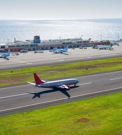 Aerial view of Funchal international airport with planes by terminal building, airplane taking off at air field, seascape in background in bright sunshine, Funchal, Madeira island, Portugalのeditorial素材