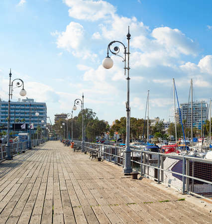 Wooden pier of marina with moored yachts and motorboats, hotels and apartments buildings in bright evening sunshnie, Larnaca, Cyprusのeditorial素材