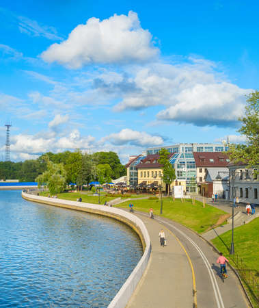 MINSK, BELARUS - JULY 17, 2019: People walking and cycling by Svisloch river embankment in bright sunny daytime, green park and city architecture in backgroundのeditorial素材