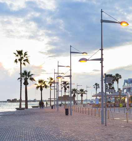 PAPHOS, CYPRUS - FEBRUARY 15, 2019: Touristic downtown embankment with souvenir shops and cafes, car, palm trees and sunset over the seaのeditorial素材