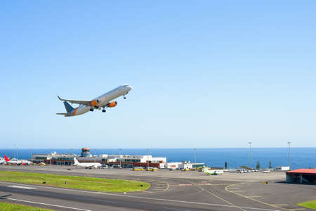 Airplane taking off International Airport skyward view, planes parked by terminal, sunshine, seascape, Funchal, Madeiraのeditorial素材