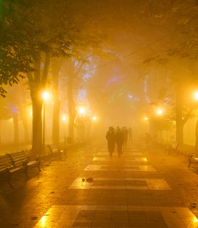 People walking at Odessa city center illuminated alley in the heavy night fog. Odessa, Ukraineの写真素材