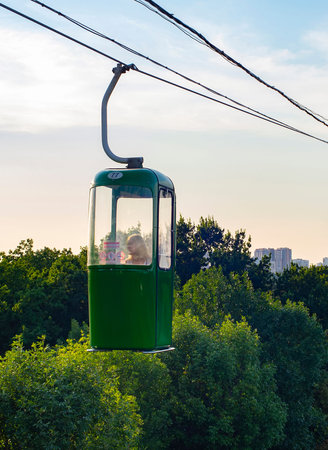 Colorful cable way over park with green trees at summer sunset, Kharkiv cityscape in background,...