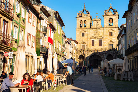 BRAGA, PORTO - NOVEMBER 14, 2021: People sitting in street cafe, Santa Cruz church in background, evening sunshineのeditorial素材