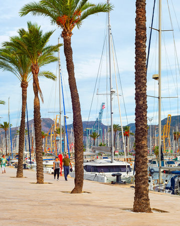 CARTAGENA, SPAIN - NOVEMBER 1, 2021: People walking at embankment with palms by marina with yachts, Cartagena, Spainのeditorial素材