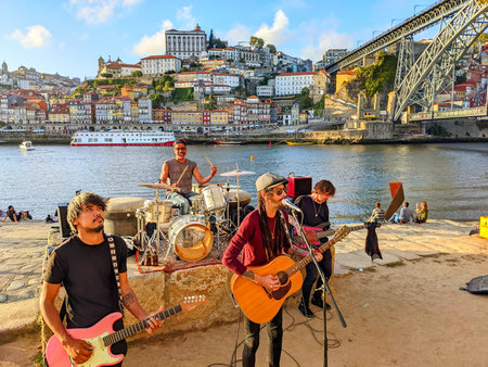 PORTO, PORTUGAL - SEPTEMBER 6, 2022: Street musicians band playing on embankment of Gaia in sunset, downtown cityscape with Ribeira and Dom Luis bridge view in backgroundのeditorial素材
