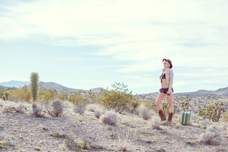 fashionable woman traveler walking with suitcase and luggage in desertの写真素材