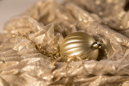 Abstract Warm Gold Christmas Globe Ornament On Shiny Fabric Background. Selective Focus With Copy Space.の写真素材