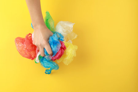 Top view female hand holding a heap of waste plastic bags on yellow background.