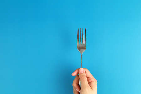 Top view female hand holding a fork on blue backgroundの写真素材