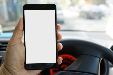 Close up adult hand holding a blank screen smartphone while driving a car.