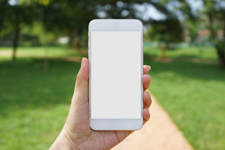 Closeup female hand holding a smartphone with an isolated screen at an outdoor park