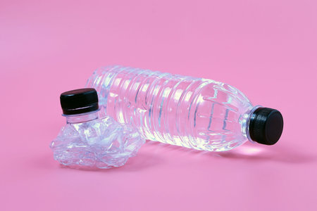 Crushed plastic drinking bottle on pink background. The idea of waste sorting, recycling and...