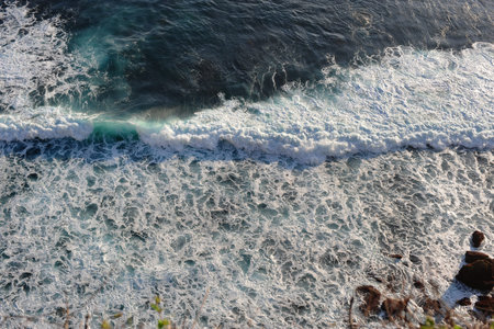 High angle view of waves breaking on Rock. Light and dark blue water foaming whilst waves break to...