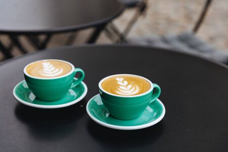 Freshly brewed coffee with heart shape on top placed in two light blue cups on saucers. Hot morning drinks served for couple on black table.の写真素材
