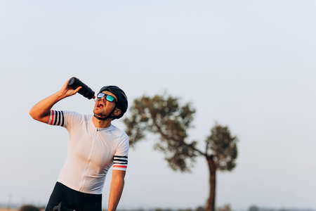 Exhausted cyclist in helmet drinking waterの写真素材