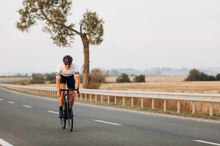 Cheerful man cycling on paved road among countrysideの写真素材