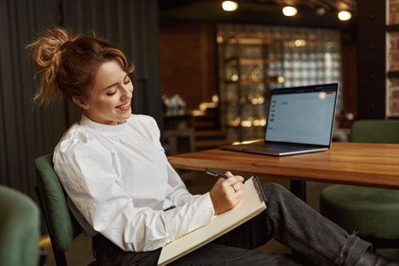Smiling woman taking notes while working on laptopの写真素材