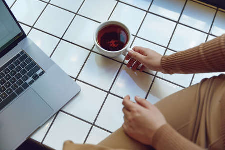 Woman sitting near window with cup of tea and laptopの写真素材