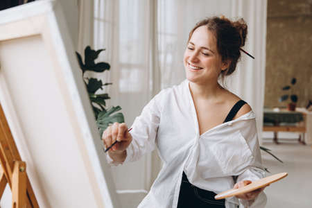 Artist painting on easel with brush and color paletteの写真素材