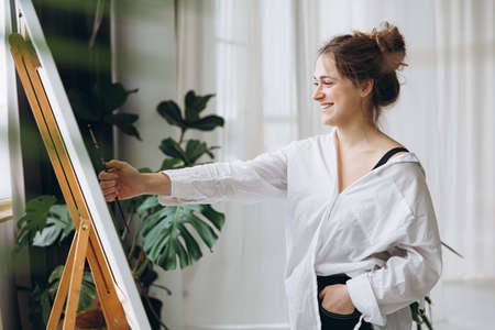 Woman using paintbrush for making measurements on canvasの写真素材
