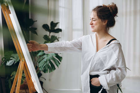 Female painter measuring proportions on easel with brushの写真素材