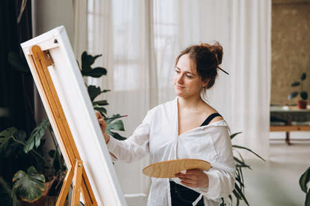 Woman standing in front of easel with palette and brushの写真素材