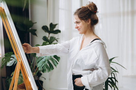 Happy woman using brush for painting on canvasの写真素材