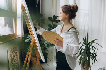 Smiling young painter drawing on canvas in studioの写真素材